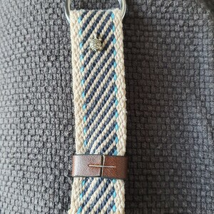 Peut inclure: Porte-cl&eacute;s tiss&eacute; avec un anneau argent&eacute;. La sangle pr&eacute;sente un fond cr&egrave;me avec des rayures diagonales bleu marine et bleu clair. Un petit charme de tortue argent&eacute; est attach&eacute;, et une bande de cuir marron s&eacute;curise la sangle.