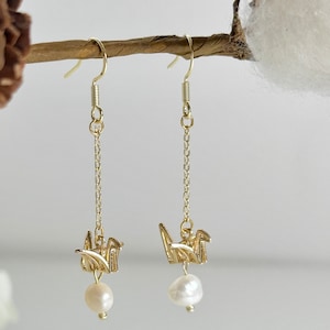 May include: Gold dangle earrings with a pearl and origami crane charm.