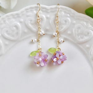 May include: A pair of delicate gold earrings with a cluster of purple flowers and pearl accents.