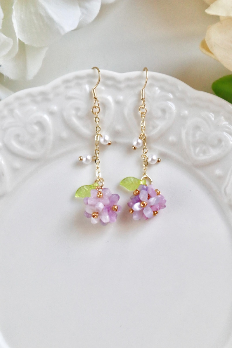 May include: A pair of delicate gold earrings with a cluster of purple flowers and pearl accents.