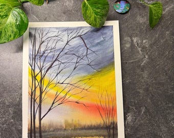 May include: Watercolor painting of a sunset over a lake, featuring silhouetted trees. The sky transitions from yellow to orange and blue. The artwork is on white paper.