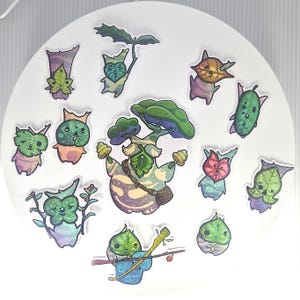 May include: A collection of eleven die-cut stickers featuring whimsical forest creatures with leaf-shaped faces and bodies in various shades of green, purple, and blue. The central sticker depicts a larger tree-like figure with a leafy canopy.