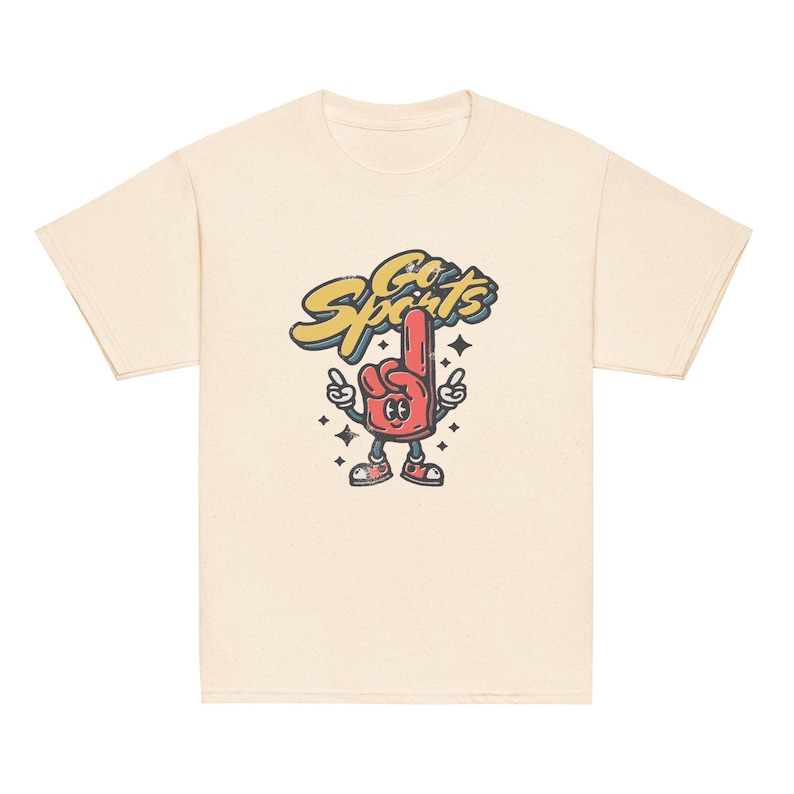 Peut inclure: Un t-shirt cr&egrave;me avec une illustration de dessin anim&eacute; d'un doigt mousse rouge avec un visage et les mots "Go Sports" en lettres jaunes.