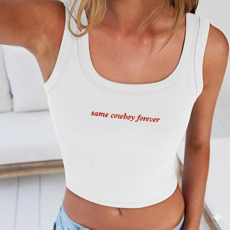 May include: White ribbed tank top with the red text "same cowboy forever". The sleeveless top has a scoop neckline and is made of a soft, comfortable material. A casual, everyday top.