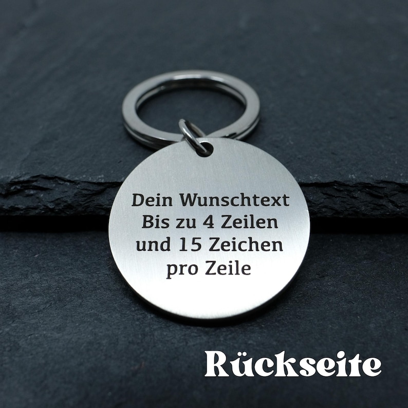 May include: A silver key chain with a round tag that says "Dein Wunschtext Bis zu 4 Zeilen und 15 Zeichen pro Zeile" and "R&uuml;ckseite" on the back.