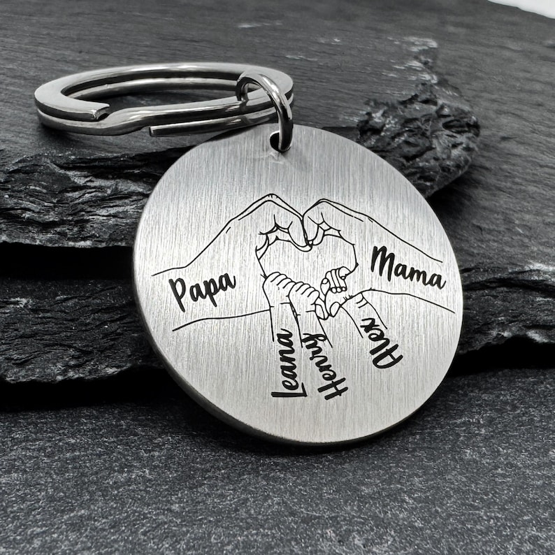 May include: Silver keychain with a heart shape formed by hands with the names Papa, Mama, Leana, Henry, and Alex engraved on it.