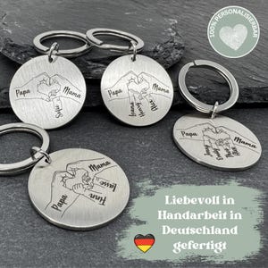 May include: Four silver keychains with interlocking hands and personalized names. Each keychain features a heart shape formed by the hands. The keychains are displayed on a gray background with the text "Liebevoll in Handarbeit in Deutschland gefertigt" and a German flag.