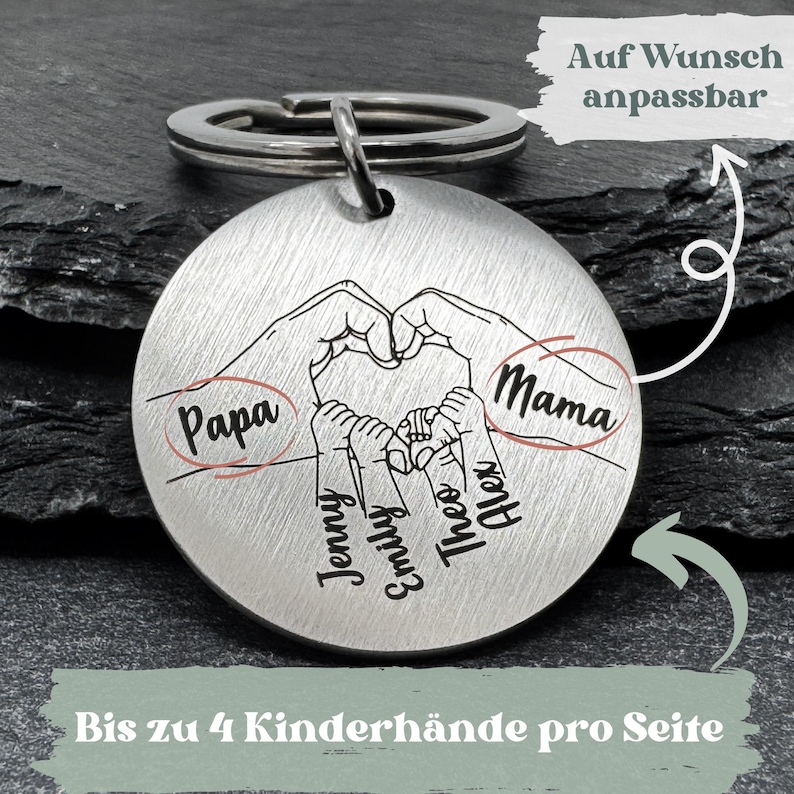 May include: Silver keychain with a heart formed by two hands, with four smaller hands inside the heart. The hands are labeled "Papa", "Mama", "Jenny", "Emily", "Theo", and "Alex". The text "Bis zu 4 Kinderh&auml;nde pro Seite" and "Auf Wunsch anpassbar" is also visible.
