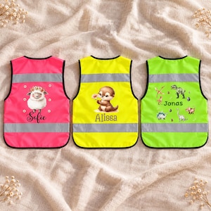 Könnte beinhalten: Drei hochsichtbare Sicherheitswesten in Pink, Gelb und Limettengrün mit reflektierenden silbernen Streifen. Die pinke Weste zeigt ein Schaf und den Namen Sofie, die gelbe einen Otter und Alissa, und die grüne Dinosaurier und den Namen Jonas.