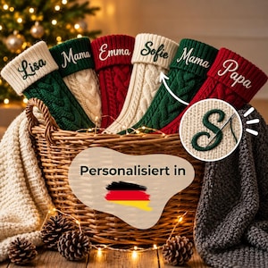 Op de afbeelding: Zes kerstsokken van kabelgebreid materiaal in rood, groen en crème, elk met een gepersonaliseerde naam geborduurd op de boord. De sokken staan in een gevlochten rieten mand, met een cirkelvormige inzet die een naald laat zien.
