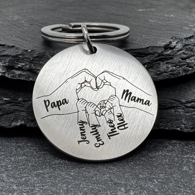 May include: Silver keychain with a heart formed by two hands, with the words "Papa" and "Mama" on either side. Inside the heart are four smaller hands with the names "Jenny", "Emily", "Theo", and "Alex" written below.