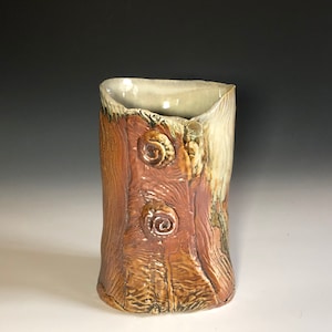 Peut inclure: Un vase en céramique avec une surface texturée ressemblant à de l'écorce d'arbre. Le vase a un glaçage brun clair et beige avec deux motifs en spirale en relief.