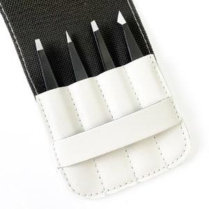 May include: A white leather case with four slots for tweezers. The case is closed and the tweezers are visible inside.