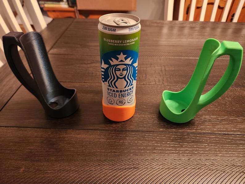 May include: A can of Starbucks Iced Energy Blueberry Lemonade with a green and orange base, next to a black and a green can holder. The can holders have a handle for easy carrying.