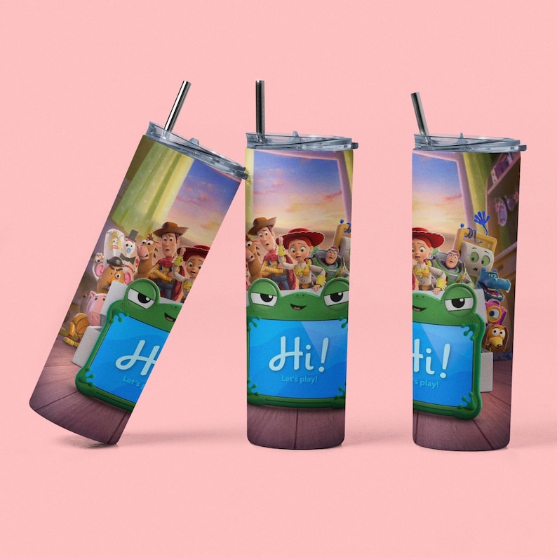 May include: Three cylindrical tumblers with lids and straws featuring a Toy Story character graphic. The design shows Woody, Jessie, and other toys behind a green frog-shaped tablet displaying the text Hi! Let's play! on a wooden floor background.