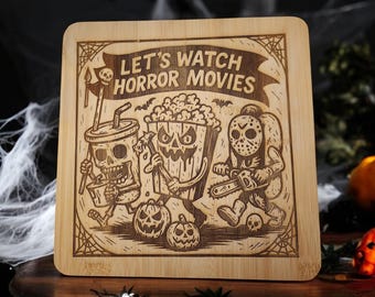 May include: A square wooden cutting board with a carved Halloween-themed design. The design features a skull in a cup, a popcorn bucket, and a figure with a chainsaw. The text "LET'S WATCH HORROR MOVIES" is above the figures.