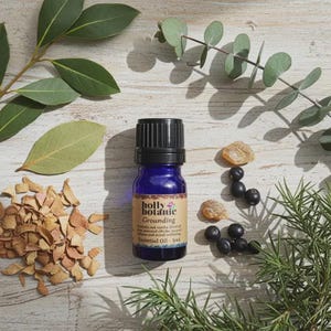 May include: A blue essential oil bottle with a black cap, labeled "Grounding" by Holly Botanic, sits among leaves, berries, and wood chips. The bottle contains 5ml of essential oil. Green and brown tones create a natural, earthy aesthetic.
