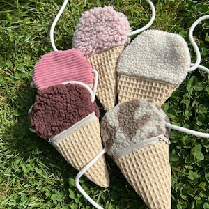 Könnte beinhalten: Vier eistütenförmige Umhängetaschen mit weißen Kordelträgern. Die Taschen haben Waffelmuster-Stoffkegel und flauschige Oberteile in Rosa, Dunkelbraun, Creme und einem braun-weiß gesprenkelten Muster, jeweils mit einem Reißverschluss oben.