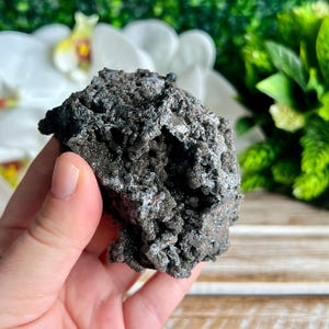 Op de afbeelding: Een grote, donkergrijze, ruwe en getextureerde steen met een kristallijne structuur. De steen heeft een metaalachtige glans en lijkt een natuurlijk mineraalmonster te zijn.