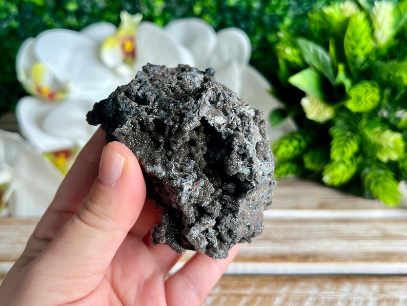 Op de afbeelding: Een grote, donkergrijze, ruwe en getextureerde steen met een kristallijne structuur. De steen heeft een metaalachtige glans en lijkt een natuurlijk mineraalmonster te zijn.
