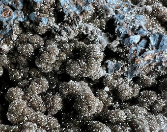 May include: Close-up of a dark gray and silver mineral specimen with a rough, textured surface. The mineral has a sparkly, crystalline appearance.