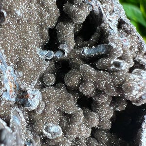 Op de afbeelding: Close-up van een donkergrijze, getextureerde rotsformatie met een ruw, onregelmatig oppervlak. De rots heeft een glinsterende, kristallijne uitstraling met kleine, witte kristallen die overal in zijn ingebed.