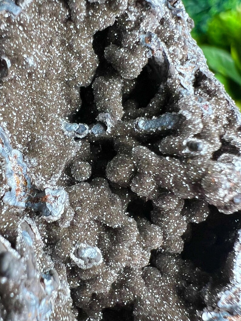 Op de afbeelding: Close-up van een donkergrijze, getextureerde rotsformatie met een ruw, onregelmatig oppervlak. De rots heeft een glinsterende, kristallijne uitstraling met kleine, witte kristallen die overal in zijn ingebed.