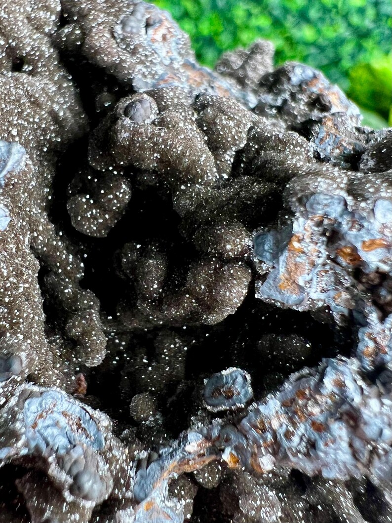 Op de afbeelding: Close-up van een donkergrijze, getextureerde steen met een zilveren, iriserende glans. De steen heeft een ruw, onregelmatig oppervlak met veel kleine, onregelmatige vormen.