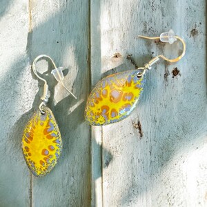 May include: A pair of yellow and blue abstract swirl earrings with silver hooks.