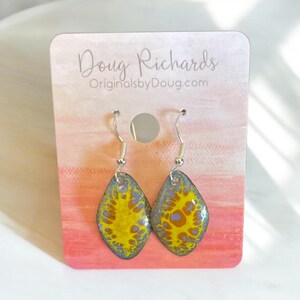 May include: A pair of yellow and blue enamel earrings with a silver hook. The earrings are shaped like a teardrop and have a marbled pattern.