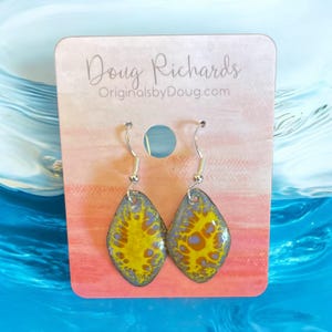 May include: A pair of silver dangle earrings with a yellow and blue abstract design. The earrings are on a white card with the text "Doug Richards OriginalsbyDoug.com".