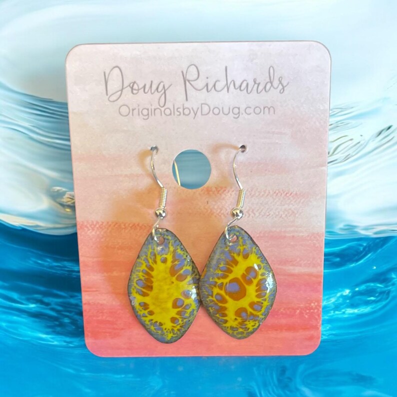May include: A pair of silver dangle earrings with a yellow and blue abstract design. The earrings are on a white card with the text "Doug Richards OriginalsbyDoug.com".
