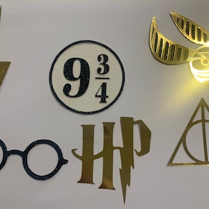 May include: A set of seven gold and black Harry Potter themed cutouts. The cutouts include a lightning bolt, a circle with the number "9 3/4" inside, a pair of round glasses, the letters "HP" with a lightning bolt, a golden snitch, and a triangle with a circle inside.