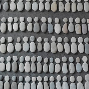 May include: A pattern of gray and white stones arranged in rows to form a series of figures. Each figure is made up of three stones, with the middle stone being slightly larger than the two on either side.