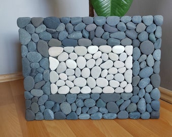 May include: A gray and white stone bath mat with a rectangular frame of gray stones and a center filled with white stones.