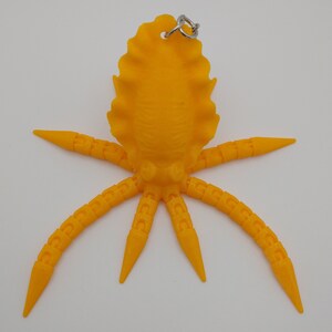 May include: A bright yellow octopus keychain with a textured surface and eight tentacles. The octopus has a small loop at the top for attaching to a bag or keys.