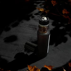 Peut inclure: Une bouteille roll-on en verre brun fonc&eacute; avec un bouchon argent&eacute; et un dessus noir. La bouteille est partiellement &eacute;clair&eacute;e, avec une bande blanche sur le c&ocirc;t&eacute;. Le bouchon a une bille roulante argent&eacute;e. Le fond est sombre avec des feuilles.