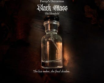 Può includere: Un flacone di profumo in vetro trasparente con tappo nero, che riporta il testo Freyja's Daughters Black Mass The Threshold e The last ember, the final shadow. Il flacone presenta un tubicino spray interno visibile e forma cilindrica.