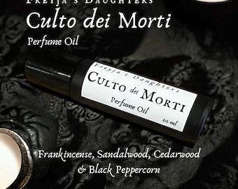 Può includere: Un flacone di vetro nero con un'etichetta bianca che recita "Freyja's Daughters Culto dei Morti Perfume Oil 10 ml". Il flacone è appoggiato su una superficie nera con il testo "Frankincense, Sandalwood, Cedarwood & Black Peppercorn" stampato sotto.