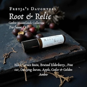 May include: A perfume oil bottle labeled "Root & Relic" from Freyja's Daughters, part of the Gothic Hauntlands Collection. The label lists ingredients like Black Spruce Resin, Bruised Elderberry, and Golden Amber. The bottle is on a dark, textured surface.