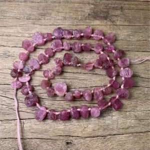 May include: A strand of pink tourmaline beads, each bead is faceted and has a unique shape. The beads are strung on a thin thread and are ready to be used for jewelry making.