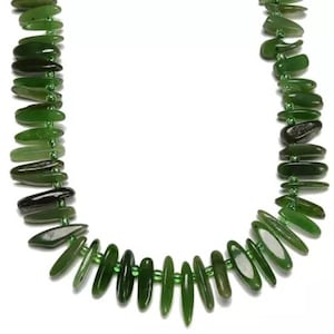 Puede incluir: Un collar de jade verde con cuentas largas, delgadas y planas. Las cuentas están enhebradas en un alambre delgado y están dispuestas en un patrón escalonado.