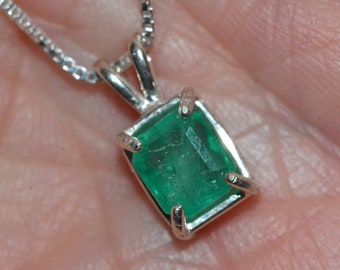 Op de afbeelding: Een zilveren ketting met een groene smaragd hanger.
