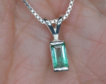 Op de afbeelding: Een zilveren ketting met een klein, rechthoekig hanger van smaragdgroene edelsteen.