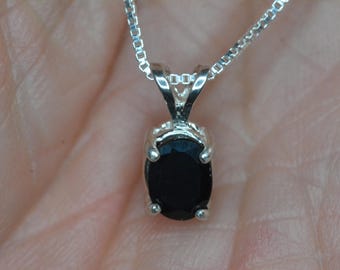 Op de afbeelding: Een zilveren ketting met een hanger met een zwarte ovale edelsteen.