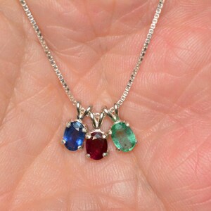 May include: A silver chain necklace with three oval-shaped gemstones: a blue sapphire, a red ruby, and a green emerald.