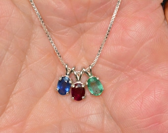Op de afbeelding: Een zilveren ketting met drie ovale edelstenen: een blauwe saffier, een rode robijn en een groene smaragd.