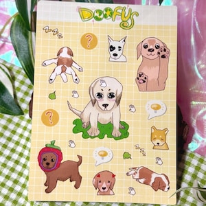 May include: A rectangular sticker sheet with a yellow grid background featuring the text Doofys at the top. The sheet contains various cartoon dog illustrations, including a puppy on green grass, a dog in a strawberry hat, and sleeping dogs.