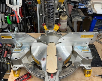 May include: A silver DeWalt miter saw with a wooden piece in the cutting area. The saw is on a wooden table with a red multi-tool.