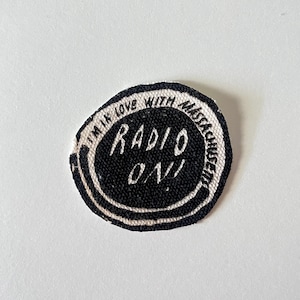 May include: A black and white fabric patch with the text "I'm in love with Massachusetts" and "Radio On!" in a circle.